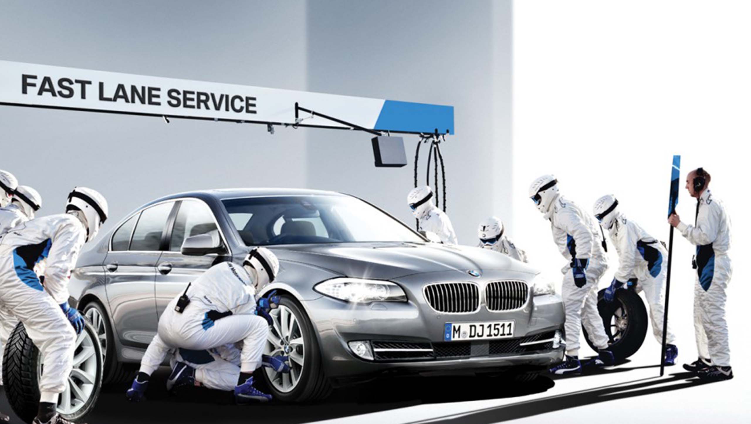 보호복을 입은 정비 인력이 은색 BMW 세단 주변에서 타이어 교체 작업을 하는 모습