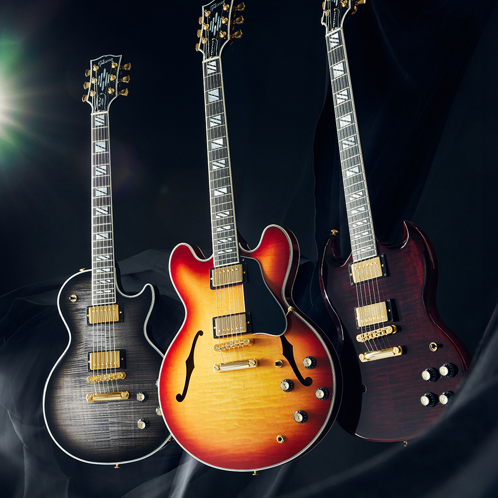 검은 천 배경 앞에 세워진 검정, 선버스트, 짙은 적색 Gibson 기타 세 대 어두운 배경 앞에 놓인 세 대의 Gibson 기타