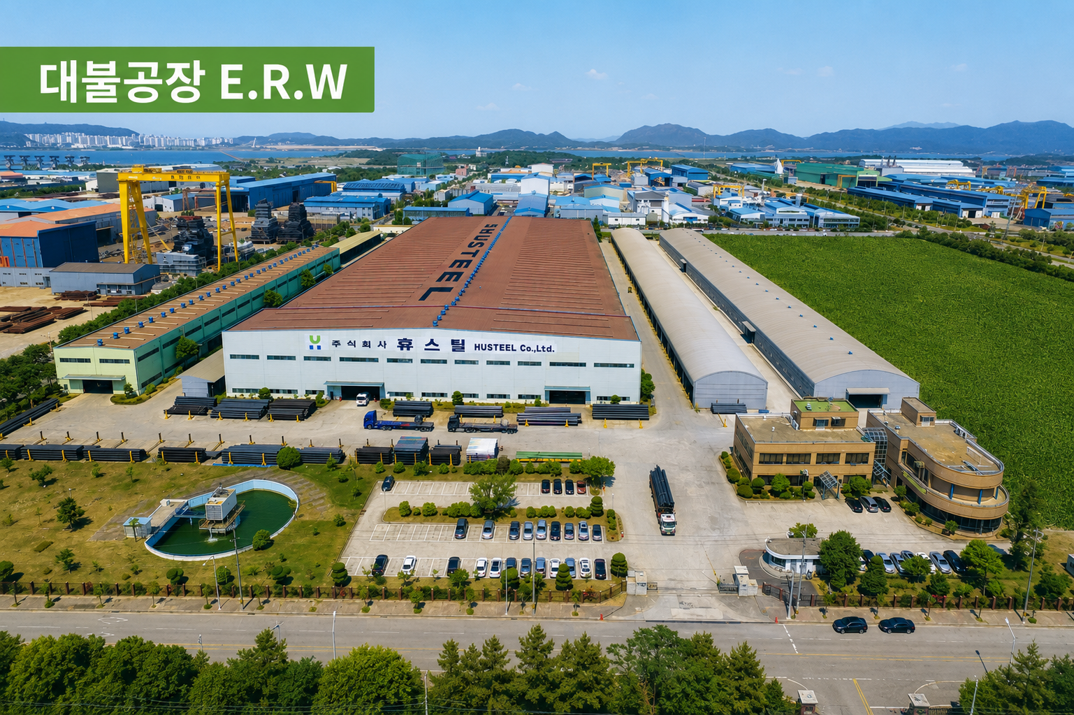 대불공장 생산동과 야적된 강관 대불공장 부지의 대형 갈색 지붕 생산동, 적재된 강관과 운송 차량을 담은 항공 사진