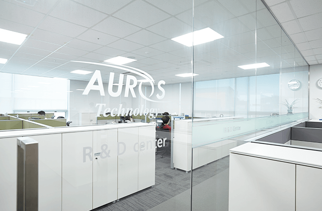 오로스테크놀로지 R&D 센터 내부 유리 벽 너머로 AURUS Technology R&D center 글자가 보이는 사무·연구 공간