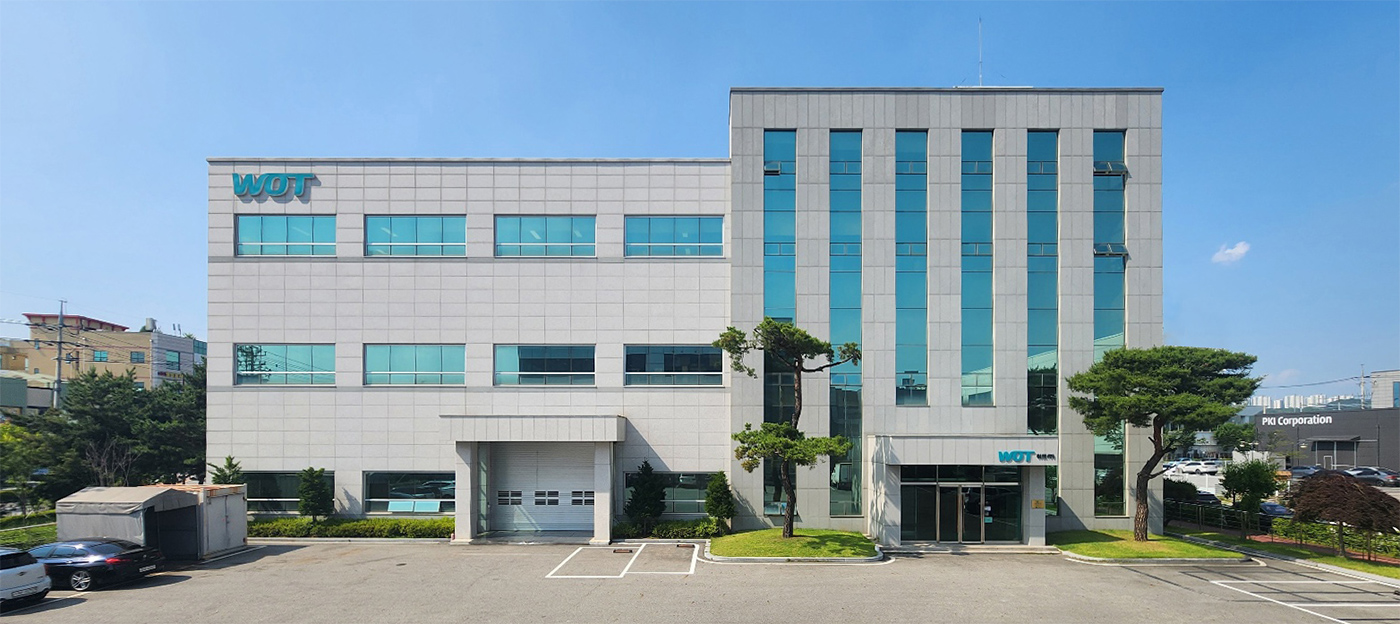 워트 사업장 건물 전경 워트 로고가 설치된 회색 외장과 청록색 창의 회사 건물 전경