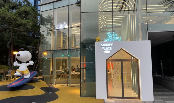 스누피 조형물과 SNOOPY PLACE 입구가 있는 문화·레저 공간 외관 유리 외벽 건물 앞에 서핑보드 위 스누피 조형물과 SNOOPY PLACE 입구가 보이는 모습